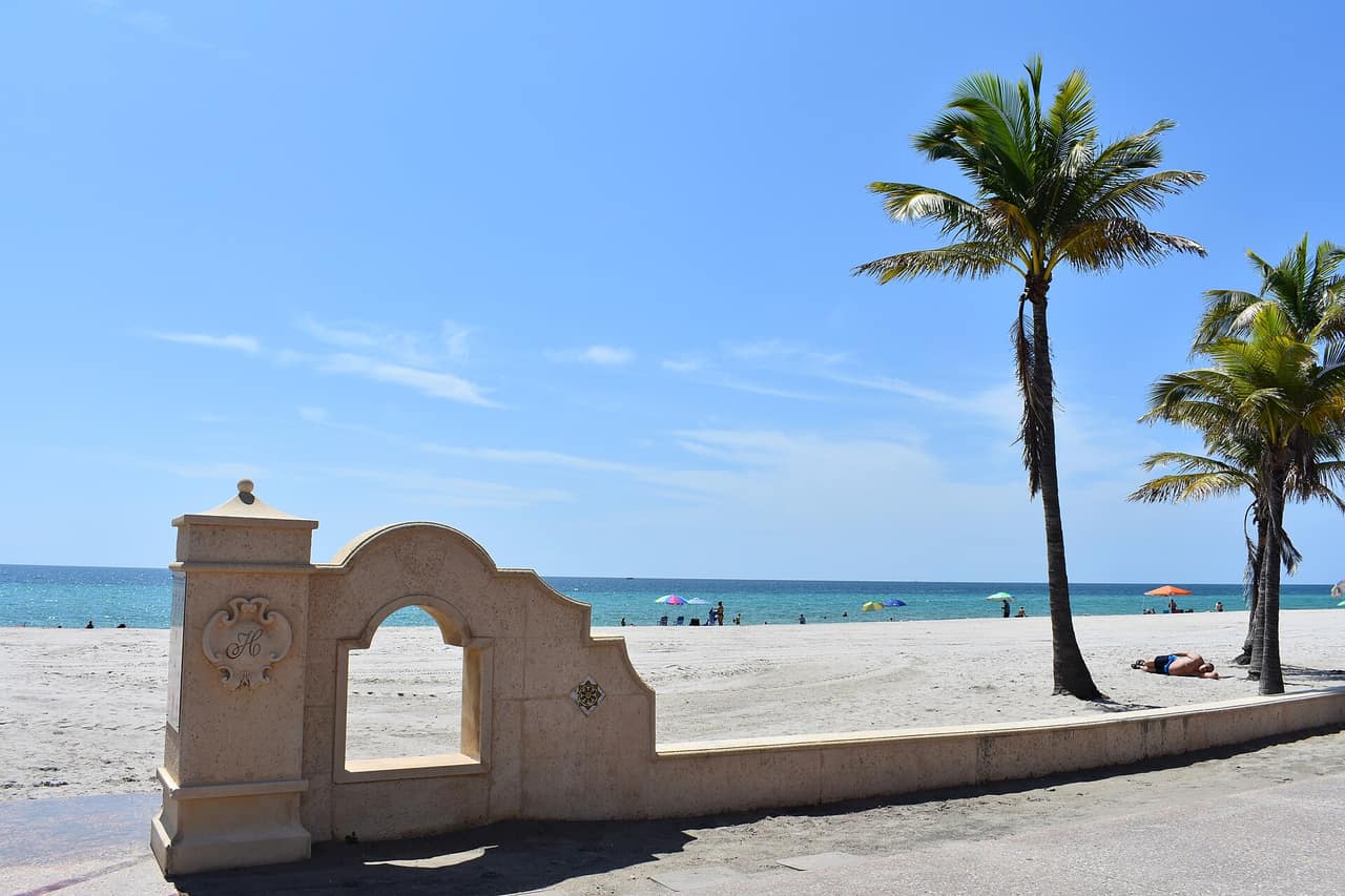 Wide sandy beach with low buildings and palms along the Broward County shoreline
